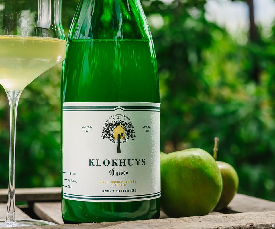 Een gevuld glas naast een fles Klokhuys op een houten kist in de boomgaard.